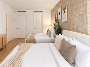 A hotel room with two beds, a wooden floor, a wall with abstract art, and a plant.