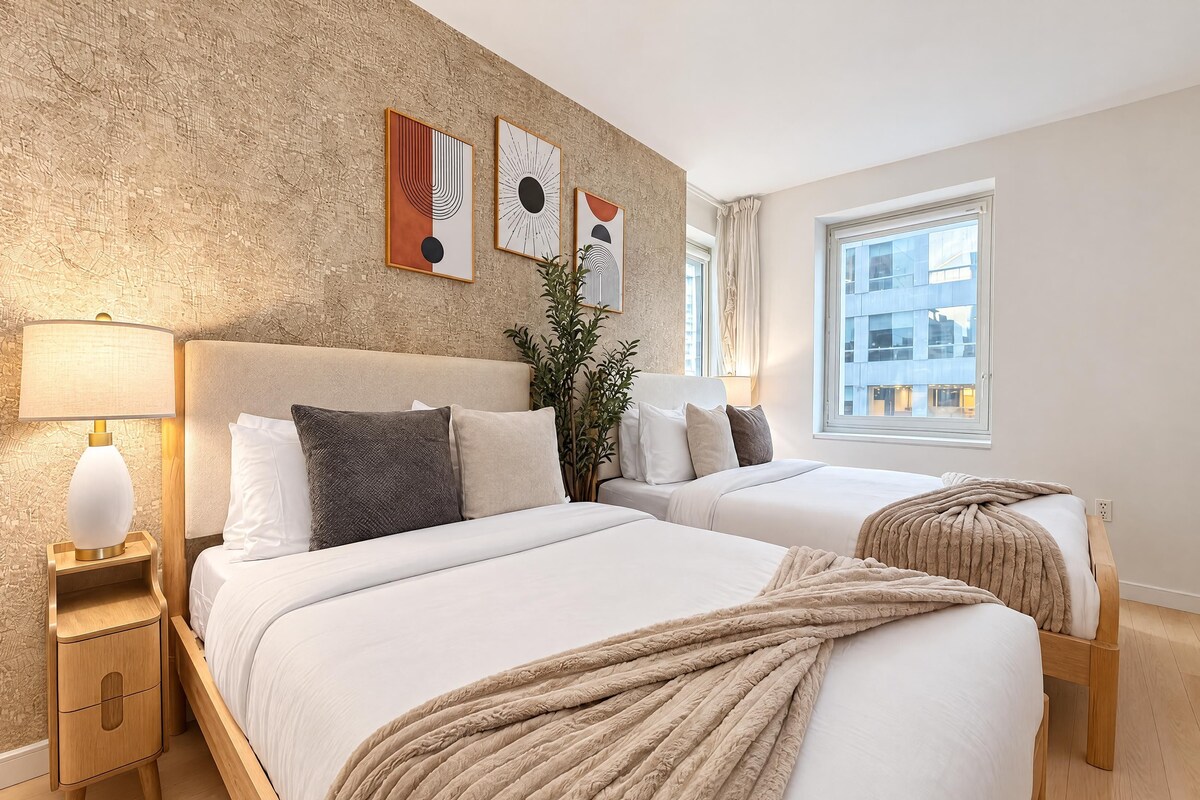 A hotel room with two beds, a nightstand, a lamp, and artwork on the wall.