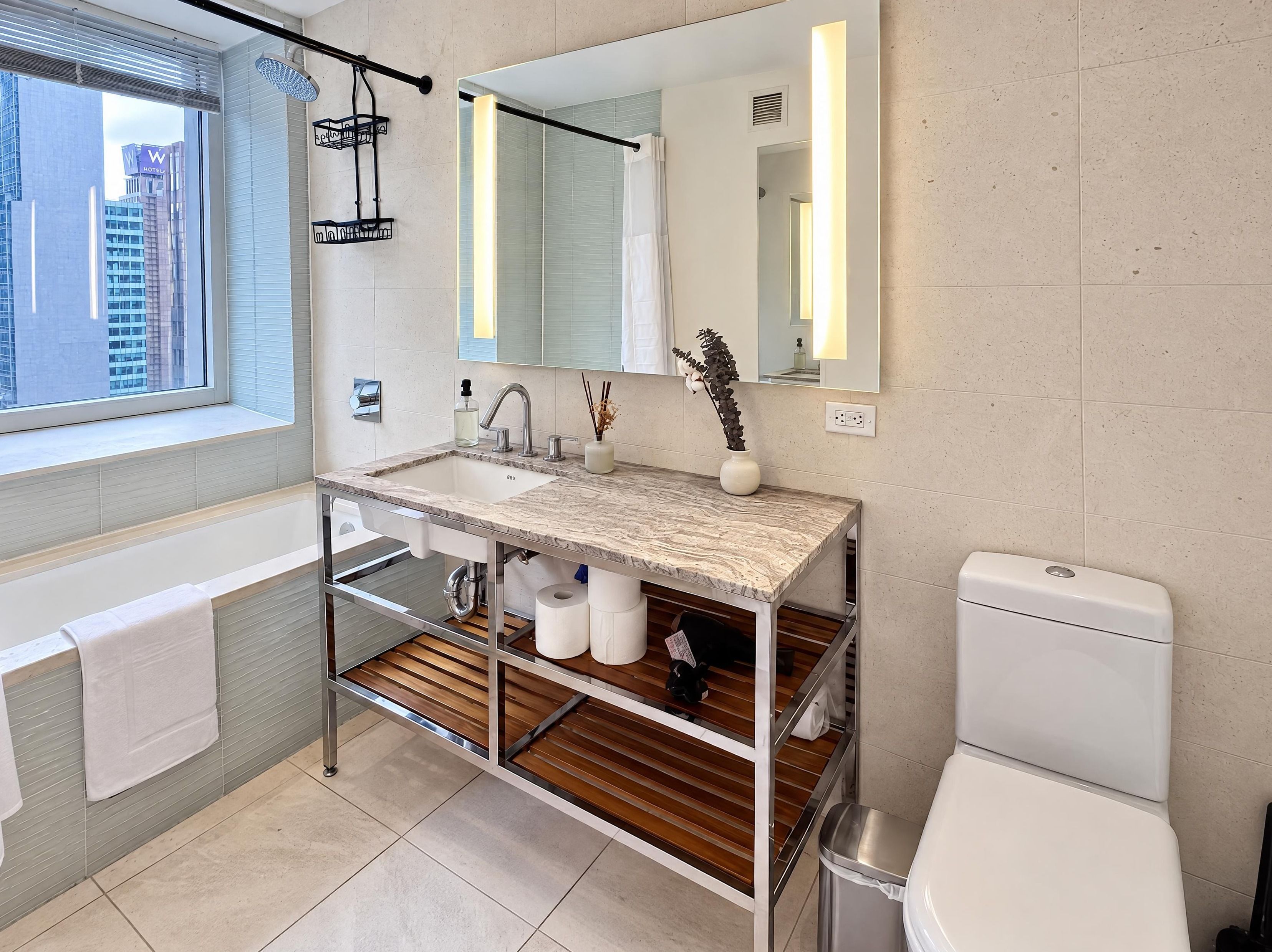 A modern bathroom with a marble sink, a large mirror, and a window with a view of buildings.