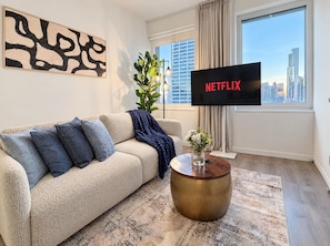 A living room with a beige sofa, a round coffee table, a flat-screen TV, and a city view.