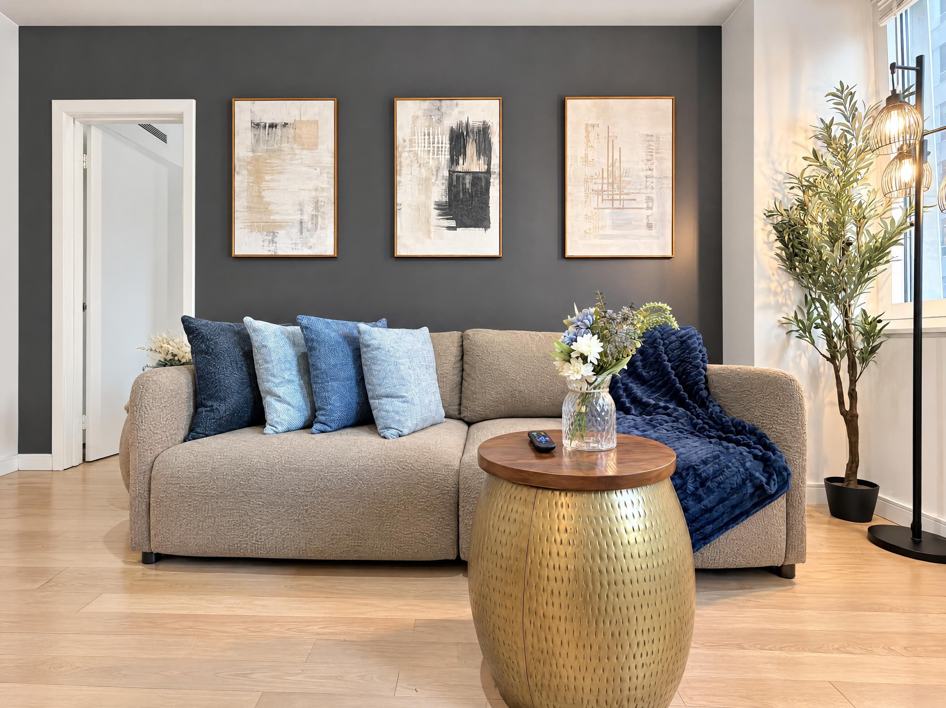 A modern living room with a beige sectional sofa, a round gold side table, and a potted plant.