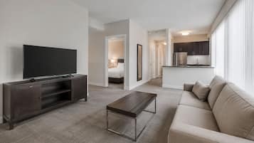 A modern living room with a flat-screen TV, a dark wooden entertainment unit, a beige sofa, and a coffee table.