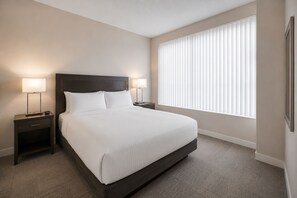 A hotel room with a large bed, two bedside tables with lamps, a window with blinds, and a carpeted floor. - Modern Manhattan Condo Near Times Square (New York)
