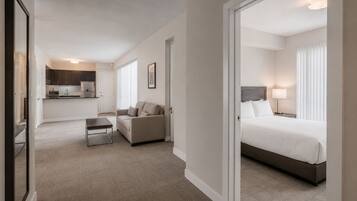 Habitación de hotel con cama, sofá, una mesita y una kitchenette al fondo.