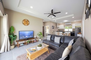 Una sala de estar moderna con un televisor de pantalla plana, un ventilador de techo y un sofá con almohadones decorativos.
