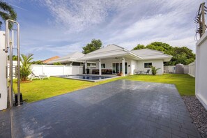 Una casa moderna con piscina, patio cubierto y césped bien cuidado.