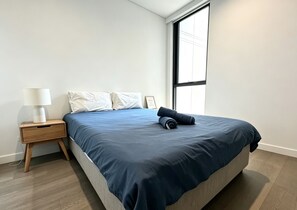 Ein modernes Schlafzimmer mit einem Bett, einem Nachttisch, einer Lampe und einem großen Fenster.