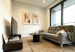 Ein stilvolles Wohnzimmer mit Flachbildfernseher, einer Couch, einem Couchtisch und zwei gerahmten Kunstwerken an der Wand.