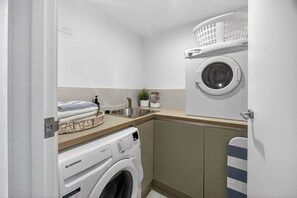 A compact laundry room with a front-loading washing machine, a drying machine, a sink, and a basket. - Sunshine Luxe Penthouse - Wide Ocean Views (Sunshine Beach)