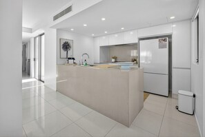A modern kitchen with a central island, white cabinetry, and a stainless steel refrigerator. - Sunshine Luxe Penthouse - Wide Ocean Views (Sunshine Beach)