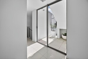 A modern interior with a glass door leading to an outdoor area, a staircase, and a potted plant. - Sunshine Luxe Penthouse - Wide Ocean Views (Sunshine Beach)