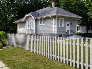 Ein zweistöckiges Haus mit weißem Zaun, einer Veranda und einem Schornstein.