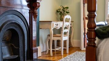 A room with a fireplace, a white chair, a small table with a vase, and a patterned rug.