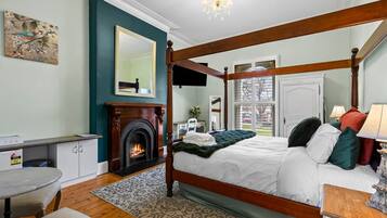 A four-poster bed with a fireplace, a desk with a chair, and a view of the outdoors through a window.