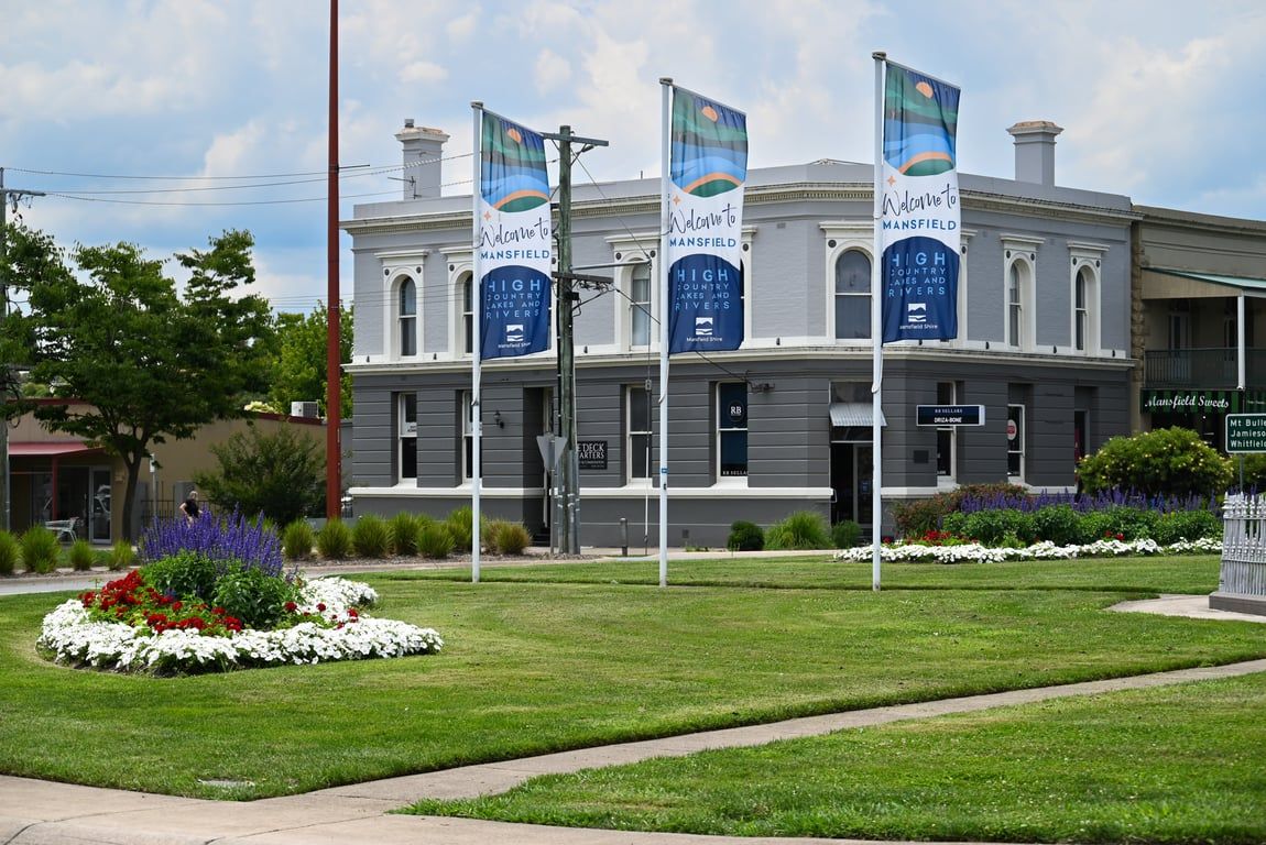 A historic building with flags, a landscaped garden, and a sign for Mansfield High Country Lakes and Rivers.