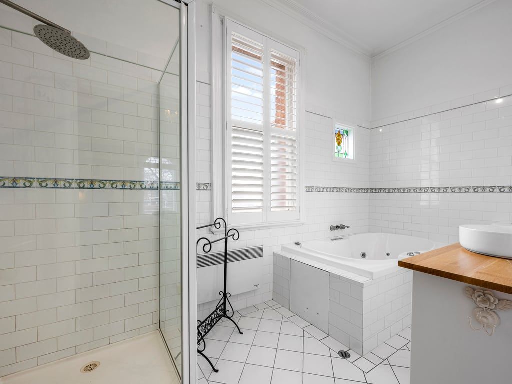 A bathroom with a glass shower enclosure, a bathtub, and a window with blinds.
