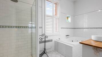 A bathroom with a glass shower enclosure, a bathtub, and a window with blinds.