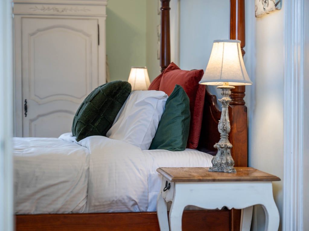 A bedroom with a bed, pillows, a bedside table with a lamp, and a door in the background.