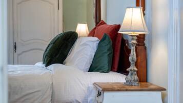 A bedroom with a bed, pillows, a bedside table with a lamp, and a door in the background.