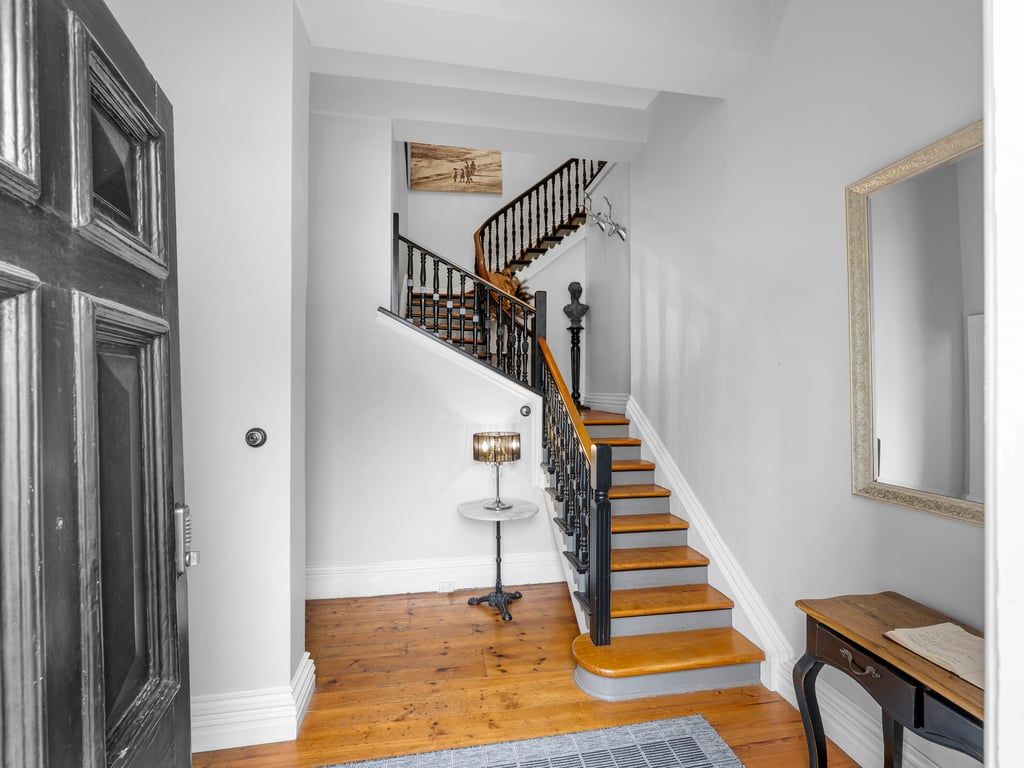 Eine Treppe mit Holzbalken und schwarzen Geländern, ein runder Tisch mit Lampe und ein Spiegel an der Wand.