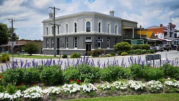 A historic building with a symmetrical facade, a central entrance, and a landscaped garden with purple and white flowers.
