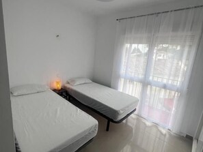 A room with two single beds, a bedside table with a lamp, and a window with curtains. - Townhouse with Year-Round Pool and Private Garage (Fuengirola)