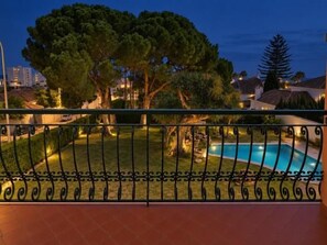 Une piscine entourée d’une clôture en métal, avec des arbres et des bâtiments en arrière-plan.