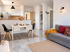 A modern living room with a sofa, a dining table with chairs, and a kitchen area in the background. - Renovated Two-Bedroom Apartment with Two Terraces and Sea Views (Benalmádena)
