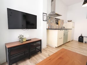 Eine moderne Küche mit Flachbildfernseher, einem Holzes Esstisch und einer kleinen Sitzecke.