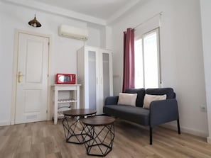 Ein kleiner, gut beleuchteter Raum mit einer Couch, einem Tisch, einer Mikrowelle und einem Kleiderschrank.