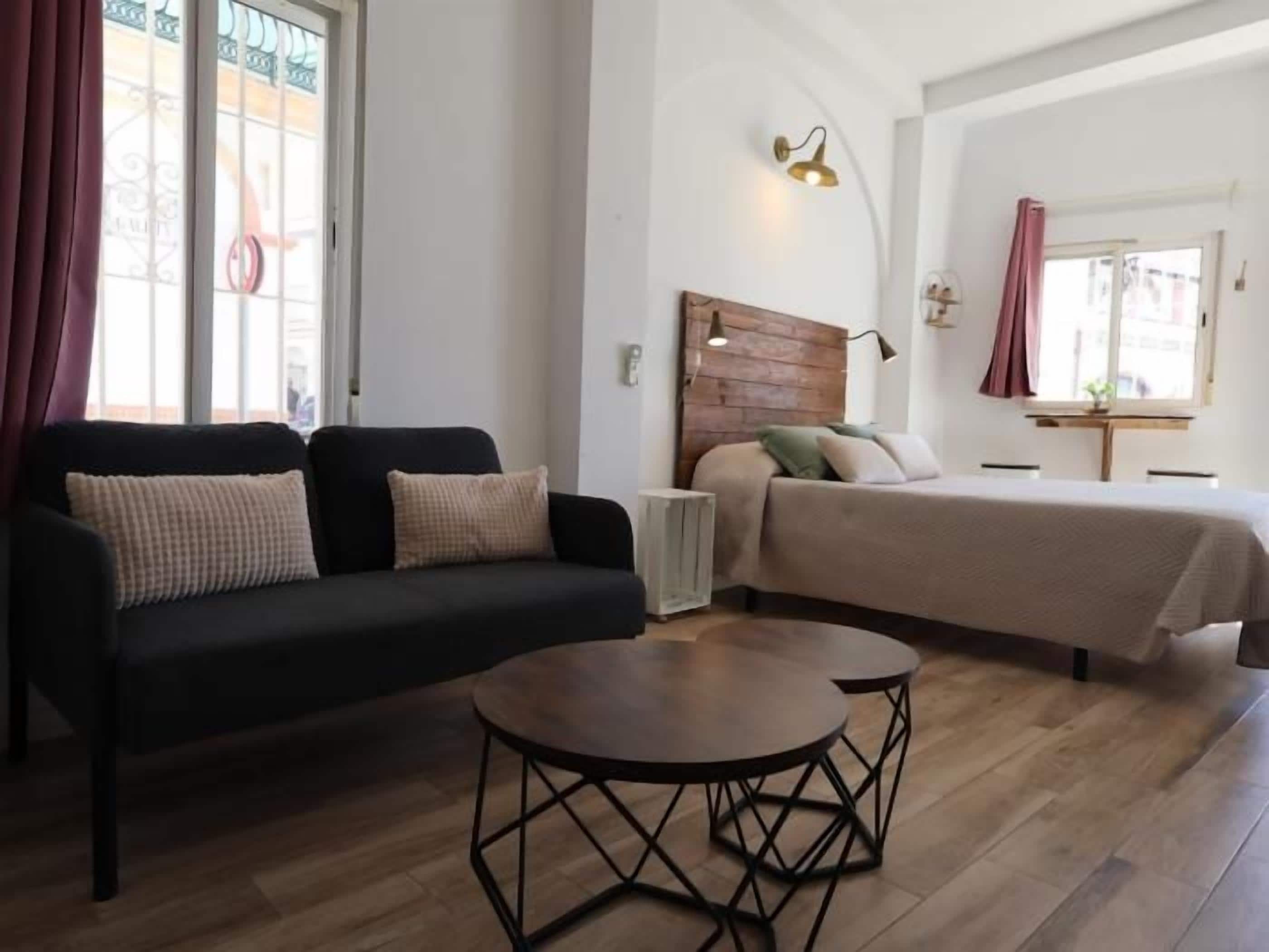 A room with a bed, a sofa, a small table, and a window with curtains.