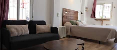 A room with a bed, a sofa, a small table, and a window with curtains.