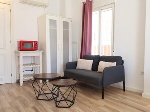 Ein Wohnzimmer mit einer Couch, zwei kleinen Tischen, einer Mikrowelle und einem Kleiderschrank.