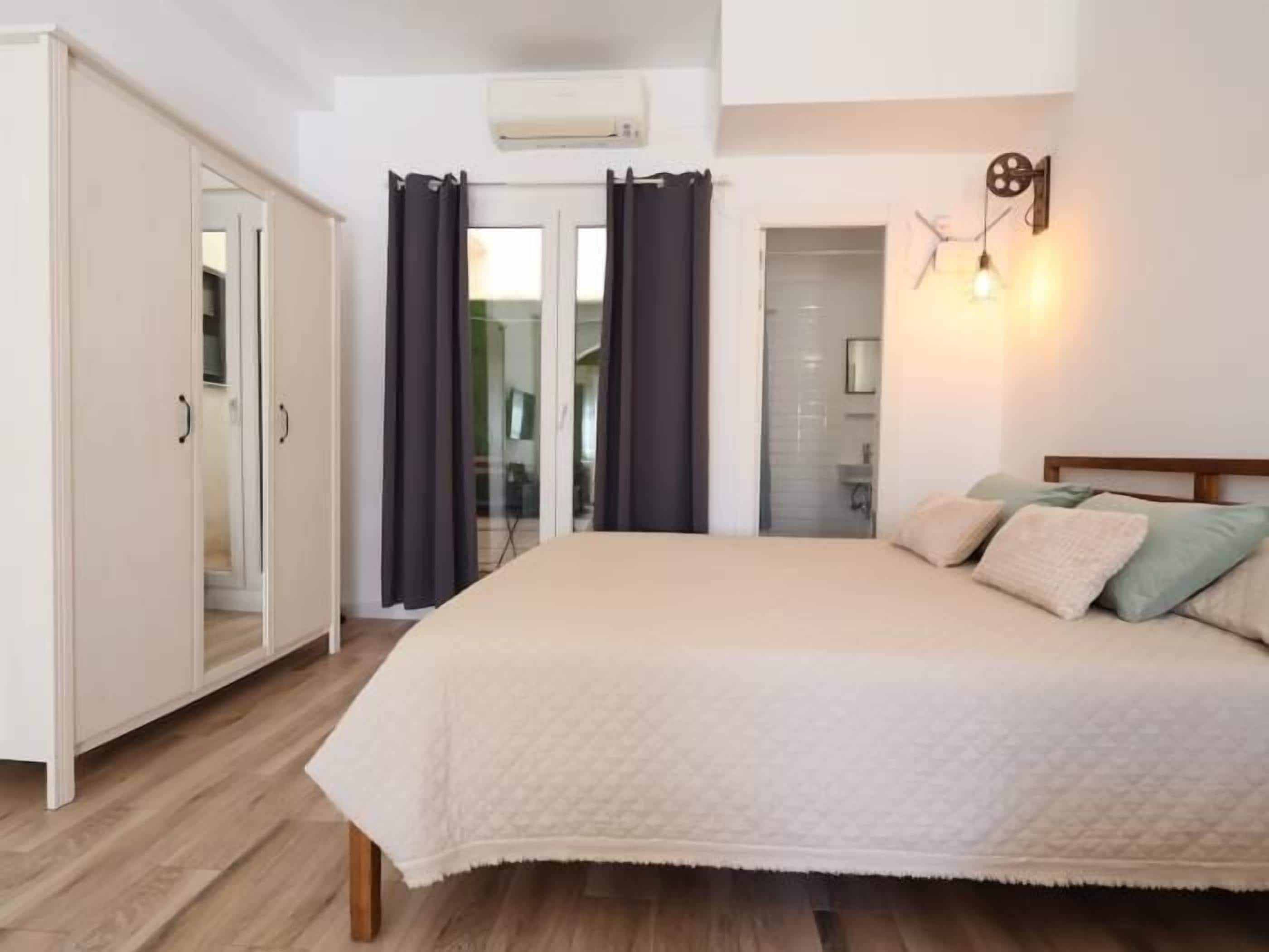 A bedroom with a bed, a wardrobe, a door, and a wall-mounted light fixture.