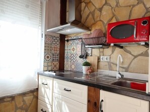 A kitchen with a stone backsplash, a microwave, a sink, and a window with blinds. - Studio with Private Patio in Arroyo de la Miel (Benalmádena)