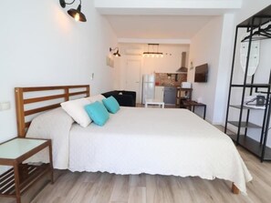 Een slaapkamer met een bed, nachtkastjes, een kledingkast en uitzicht op de keuken.