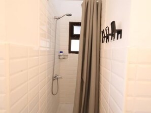 Een kleine badkamer met tegels, een douche, een handdoekhouder en een raam.