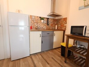 Eine kompakte Küche mit einem weißen Kühlschrank, grauen Schränken, einer Mikrowelle und einem kleinen Tisch mit einer Pflanze.