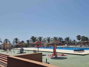 Ein Poolbereich mit Palmen, einem roten Sonnenschirm und Liegestühlen.