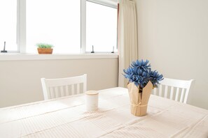 A table with a white tablecloth, a white chair, a vase with blue flowers, and a white candle on the table.