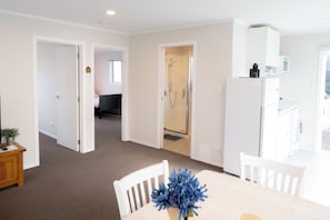 A modern kitchen with white appliances, a dining area with a table and chairs, and a visible shower area.