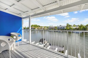 Uma varanda com vista para a água, móveis de vime branco e uma parede azul.