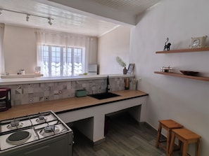 A modern kitchen with a gas stove, a window with sheer curtains, and a shelf with kitchen utensils. - Cozy villa with a pool, 5 minutes from the airport and close to all amenities (Talatamaty)