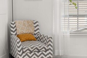 Une chaise à motifs chevrons, un coussin à motifs et une fenêtre avec des stores.