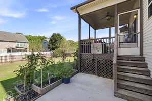 Une véranda couverte avec une balustrade en bois, un sol en béton et une vue sur un jardin arrière agrémenté d’une clôture et de verdure.