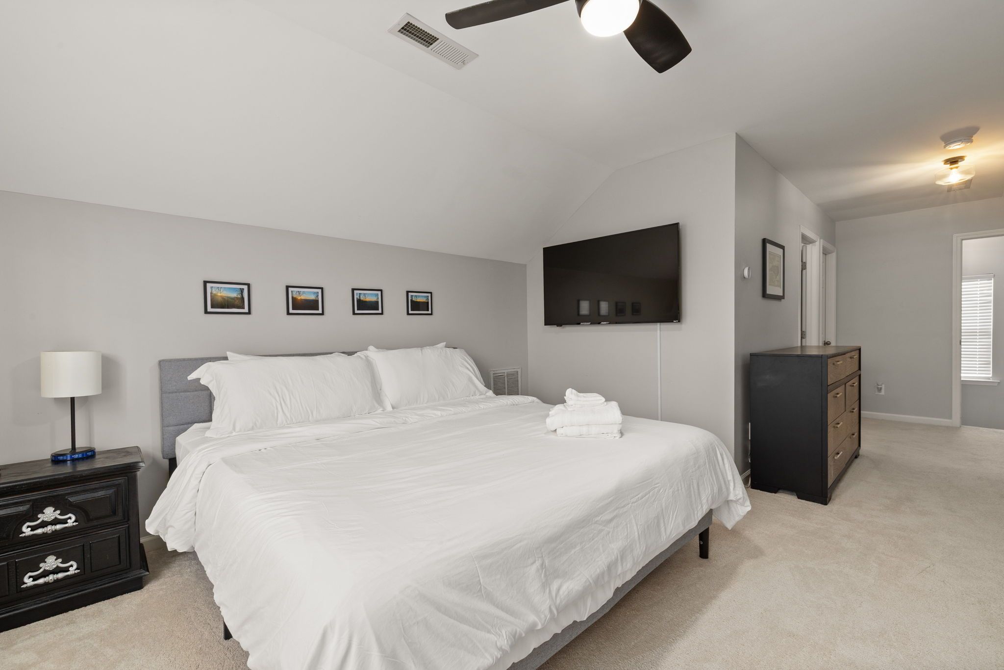 Quarto com cama, cômoda, televisão e ventoinha no teto.