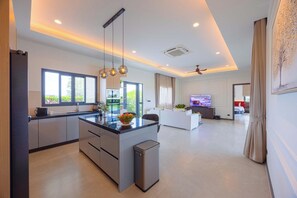 A modern living space with a kitchen, dining area, and a TV in the living room. - Modern 3BR Villa with Private Pool (NR1) (Hua Hin)