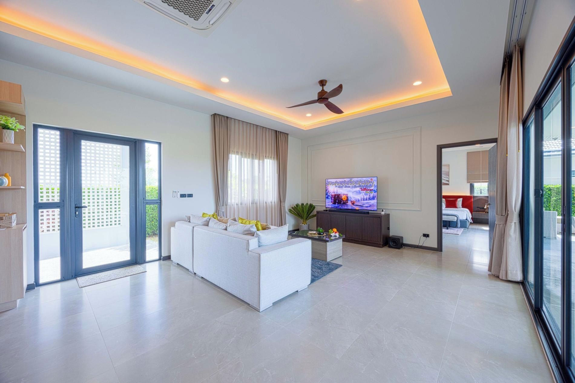 Ein modernes Wohnzimmer mit Sofa, Fernseher, Deckenventilator und Blick ins Freie.