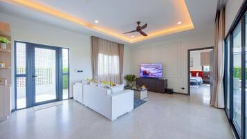 Ein modernes Wohnzimmer mit Sofa, Fernseher, Deckenventilator und Blick ins Freie.