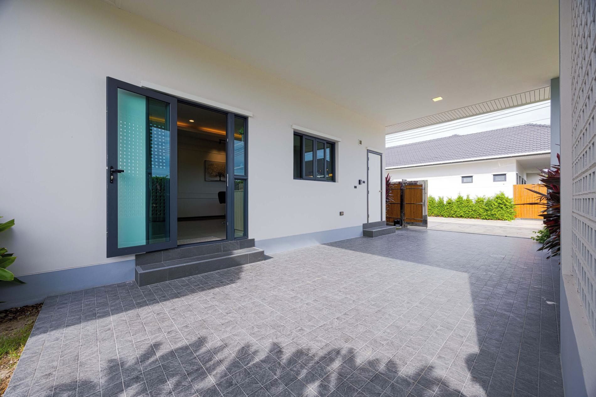 Un edificio moderno con entrada cubierta, patio con baldosas y portón de madera.